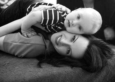 Young mother lies on bed with her baby and hugs him. Black and white image. Close up.の写真素材