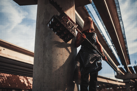 Mutant monster with weapon in form of hammer, saw and an ax. Imagination. Mutant with sack on his head.の写真素材