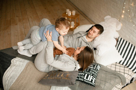 Parents lie on bed and play with their toddler. Happy young family together.