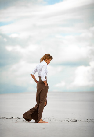Young woman goes barefoot in desert. She is dressed in long skirt and blouse.の写真素材