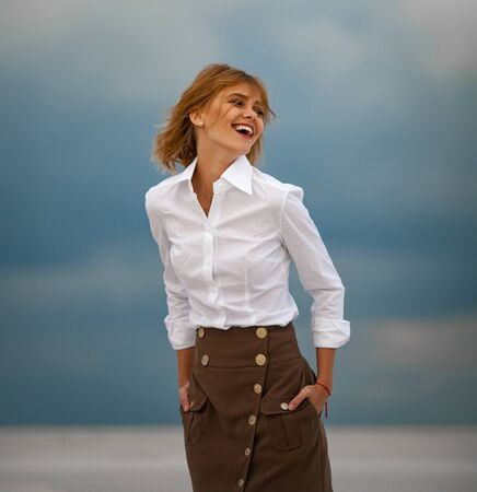Young woman stands in desert on sky background. Portrait. She is dressed in long skirt and blouse.の写真素材