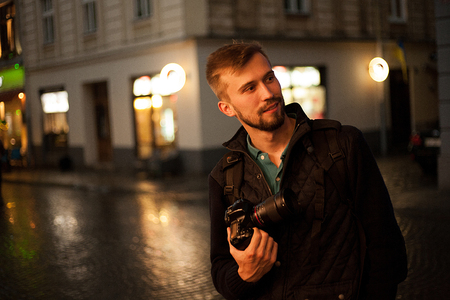 Young male photographer standing on a street in the evening. In the background there are night city lights. Self-portrait,の写真素材
