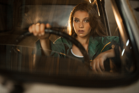 Portrait of woman driver behind steering wheel of car. View through windscreen. Reflections of light are visible on window.の写真素材