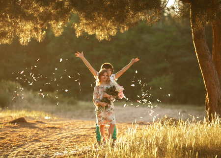 Little cheerful girl with bouquet of flowers and boy with petals in sunny glade. First love.の写真素材