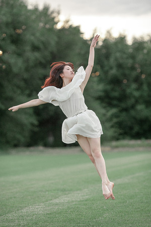 Ballerina in white dress jumping on lawn and trees background.の写真素材