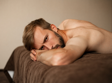 Portrait of young man topless lying on bed with brown bedsheet .の写真素材