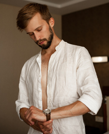 Young man in white unbuttoned shirt dresses fasten watchband.の写真素材