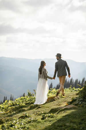 Newlyweds walk and hold hands during honeymoon trip in Carpathian mountains. Back view.の写真素材