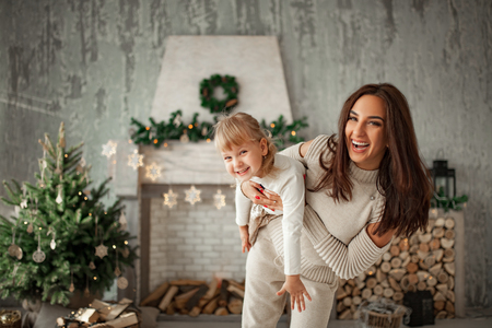 Mother and little daughter are having fun, playing and laughing cheerfully against background of Christmas tree and decorations.の写真素材
