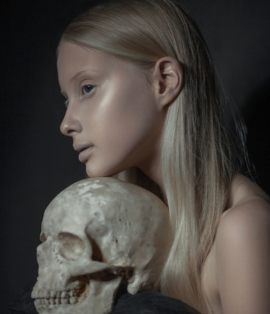 Portrait of young albino woman in profile with human skull in her hands on dark background.の写真素材