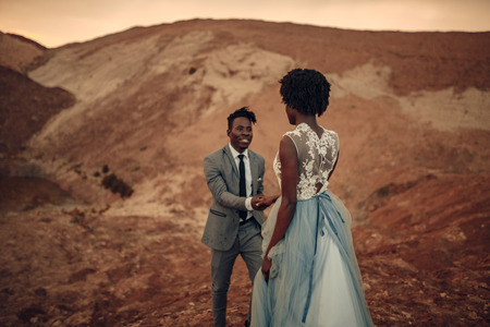 Happy newlyweds walk in canyon against beautiful landscape at sunset. Focus is on the bride.の写真素材