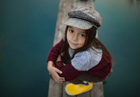 Portrait of child girl in cap and yellow boots at wooden bridge on background of river. Top view.の写真素材