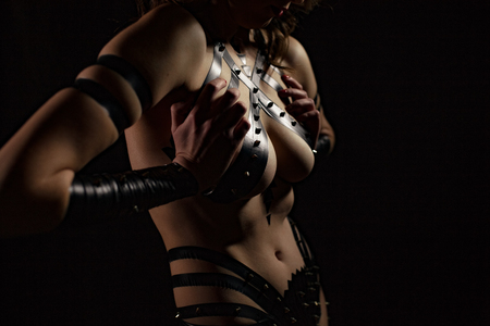 Closeup bust of Bdsm woman dressed in black costume from tape with metal spikes against black background. Concept of domination and bondage.の写真素材
