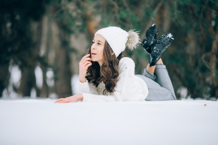 Young pensive woman is lying on the snow during the walk in the winter forest.の写真素材