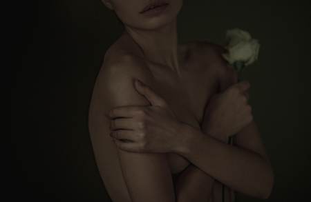 Young woman posing nude in studio with white rose in her hand. Closeup.の写真素材