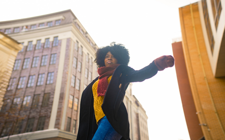 Young black woman is standing at city street against background of buildings.の写真素材