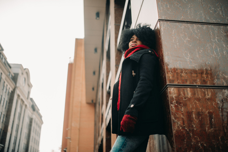 Young black woman is standing next to the building at city street.の写真素材