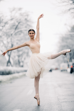 Beautiful ballerina in transparent skirt is dancing in the middle of the snowy street.の写真素材