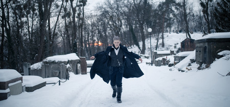 Young man in image of black magician runs on snow background.