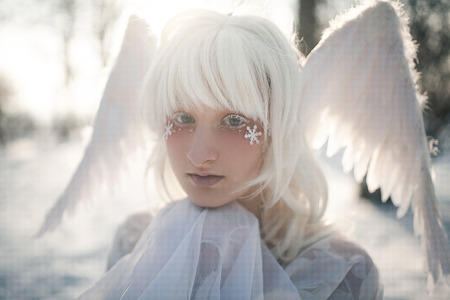 Portrait of beautiful blonde girl in image of good angel with wings dressed in white clothing.の写真素材