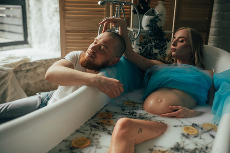 Pregnant woman takes a bath with milk, lavender herbs and orange slices next to her husband.の写真素材