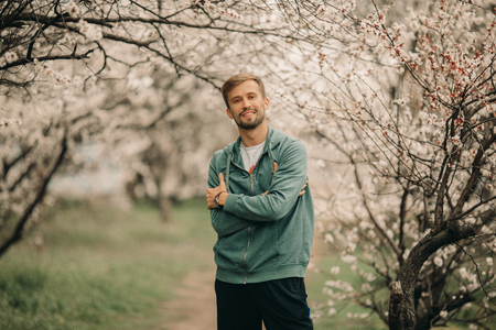 A young happy man stands among the spring blossoming apricot trees.の写真素材