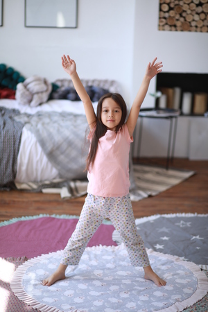 Child girl stands on the round mat and makes morning exercises.の写真素材