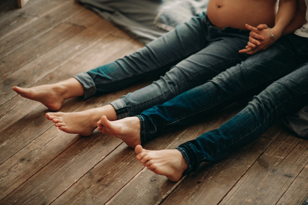 A man and his pregnant wife sit on the wooden floor and holg hands.の写真素材