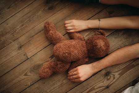 Male and female hands hold a teddy bear on background of the wooden floor.の写真素材