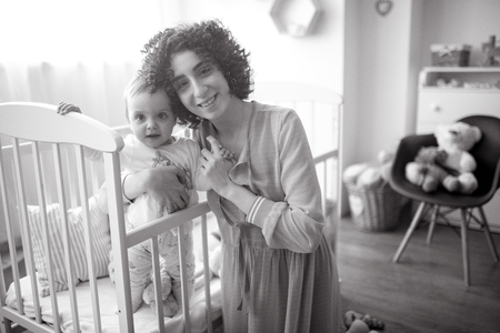 Happy mother is next her baby in the crib. Black and white image.の写真素材