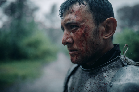 Portrait of young man in the image of a medieval knight in armor with blood and wounds on his face...