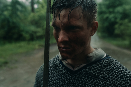Portrait of young man in the image of a medieval knight in chain armor and with a sword in his hands in rain.の写真素材