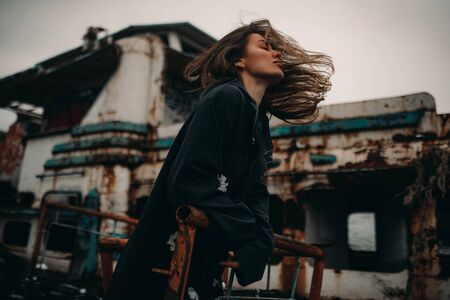 Young woman posing in coat against the background of an old abandoned rusty ship.の写真素材