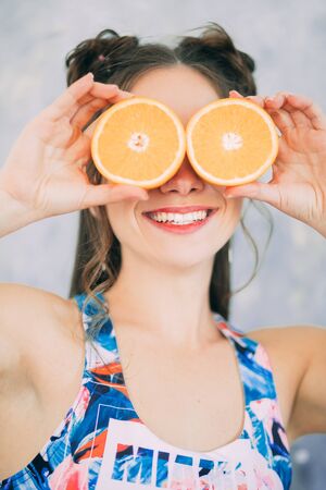 A smiling woman is holding two orange slices near her eyes. The concept of diet and healthy eating.の写真素材