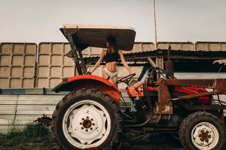 A young woman is driving a tractor in a white bikini and black t-shirt on the farm.の写真素材