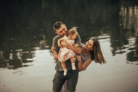 Happy parents have a fun and play with their little daughter next to the lake.の写真素材