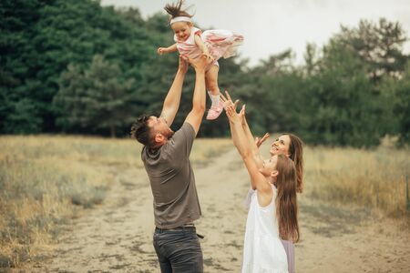 Happy family has fun on a walk and throws up their little daughter in the forest.の写真素材