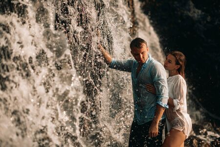 Couple in love standing and hugging under the streams of a waterfall.の写真素材