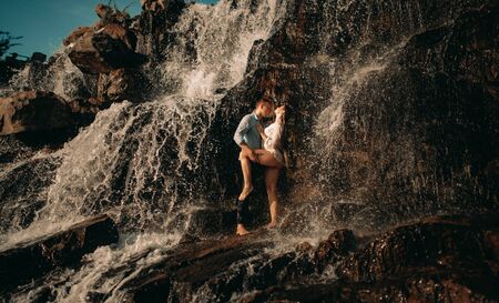 Couple in love standing and hugging under the streams of a waterfall.の写真素材