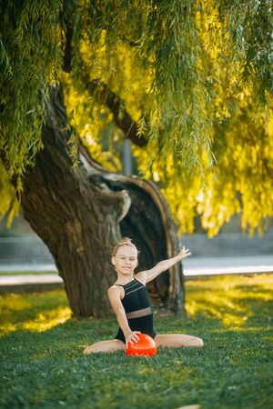 Girl gymnast performs an exercise with a ball on the lawn in the park.の写真素材