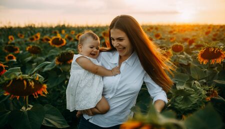 Happy young mother with baby are having a fun and walking in the sunflower field at sunset.の写真素材