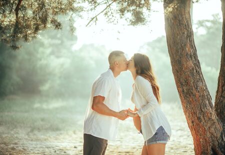 Pregnant woman is kissing with her husband during a walk in the forest on a sunny day.の写真素材
