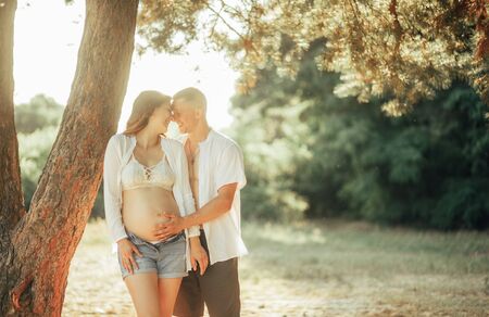 A young man touches the belly of his pregnant wife while walking through the forest.の写真素材