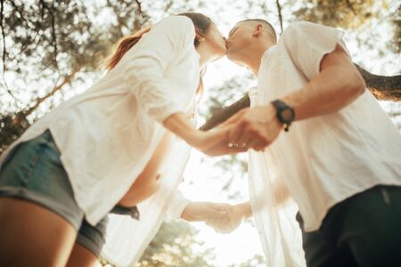 Couple with pregnant woman kisses and holds hands at the forest during walk.の写真素材