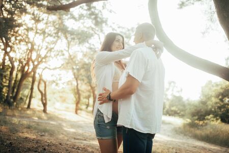 Couple with pregnant woman stands and embrace at the forest during walk.の写真素材