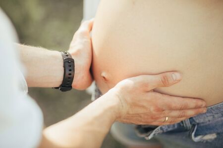 A man touches and embraces the belly of his pregnant wife during the walk. Closeup.の写真素材