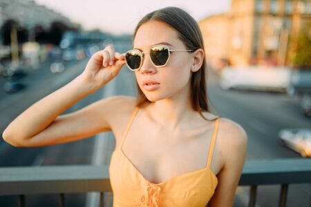 Portrait of young woman on the bridge above the road in a yellow dress and sunglasses on a...