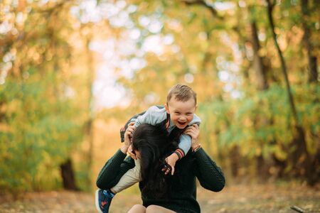 A mother and son play, have a fun and laugh while walking in the autumn forest.
