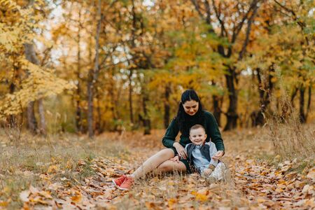 A mother and son sit on a pathway while walking in the autumn forest.