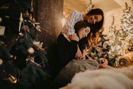 Lesbian couple sits and hugs against the background of Christmas decorations and a yellow retro car.の写真素材